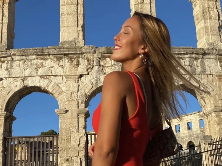 A woman in a red dress stands in front of the Colloseum in Rome.
