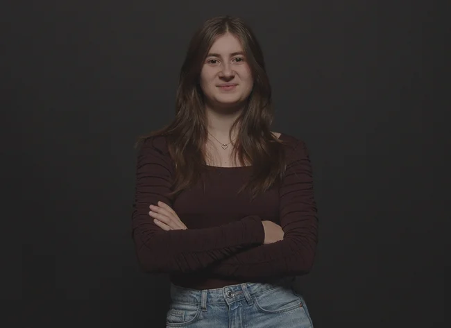 A girl smiles at the camera. She has her arms crossed.