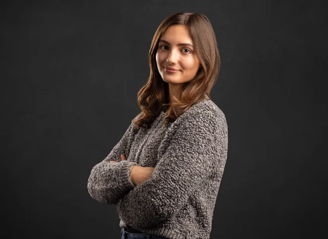 A woman with her arms crossed smiles at the camera.