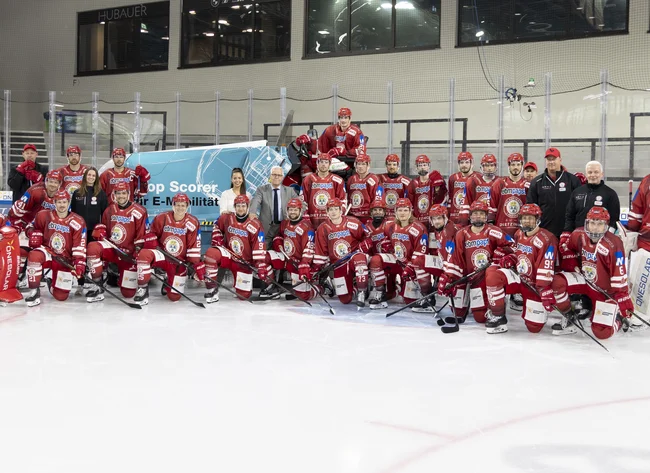 Die Eishockey Spieler des EVL und der Head of Marketing der Firma DRÄXLMAIER stehen lächelnd in der Eishockeyhalle.