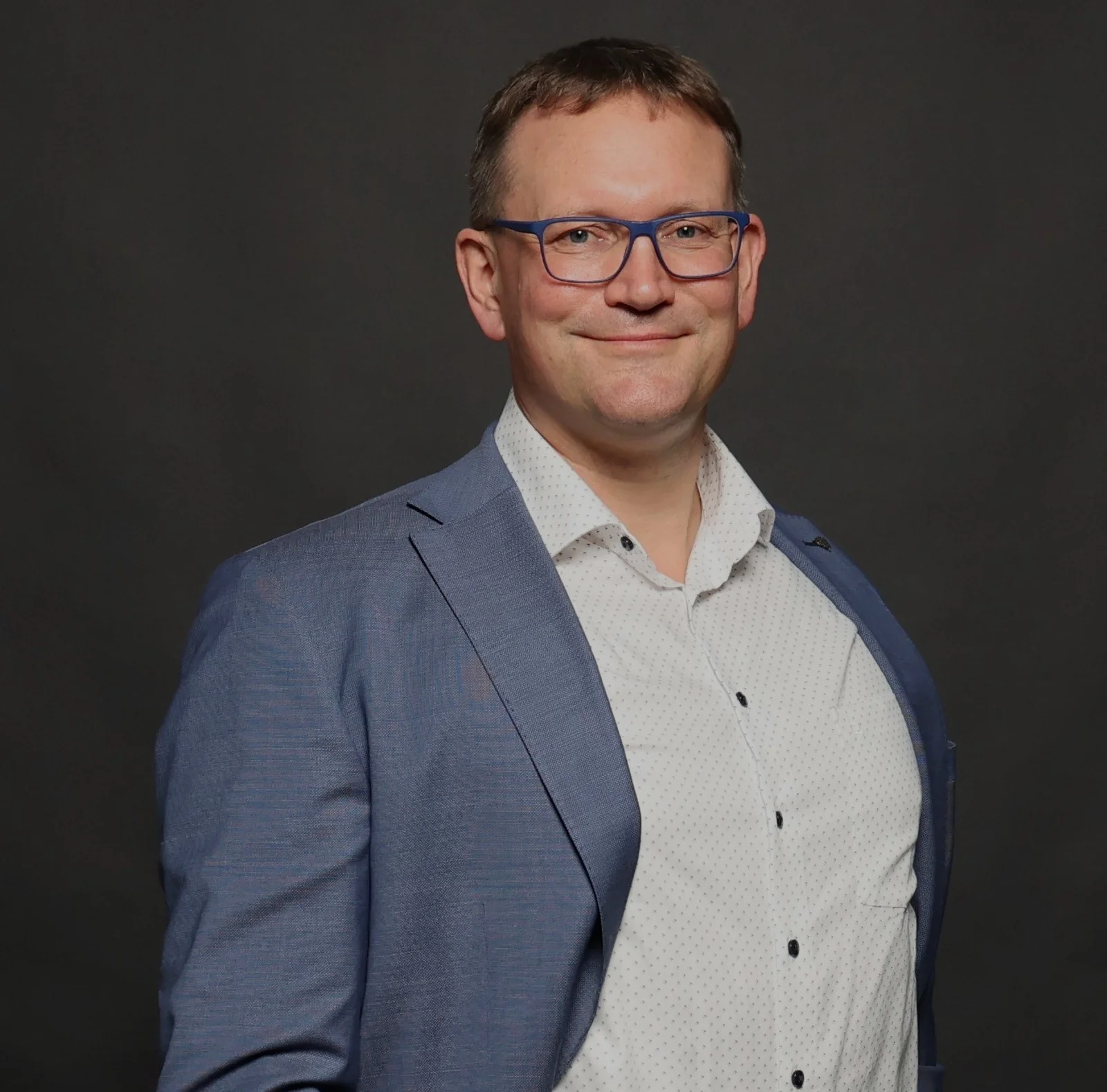 Ein Mann lächelt in die Kamera und hält seine Arme locker vor sich.