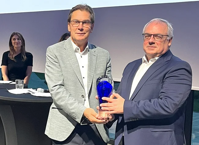 Two men smile into the camera. They are holding the Cross Border Award together. 