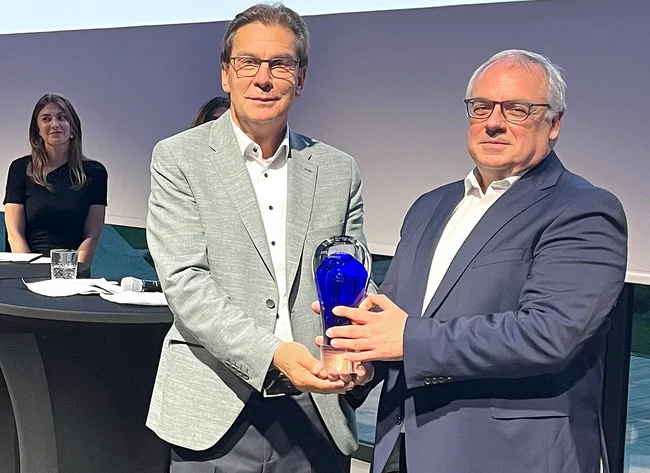 Zwei Männer lächeln in die Kamera. Sie halten gemeinsam den Cross Border Award. 