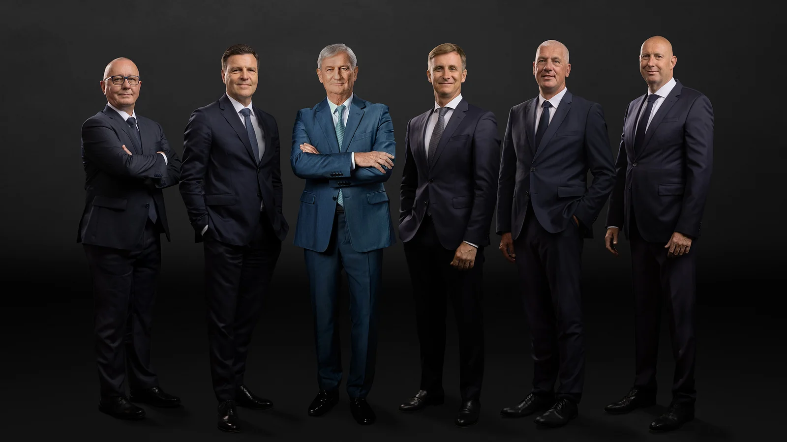 The main management in front of a black background. Six men smile into the camera. 