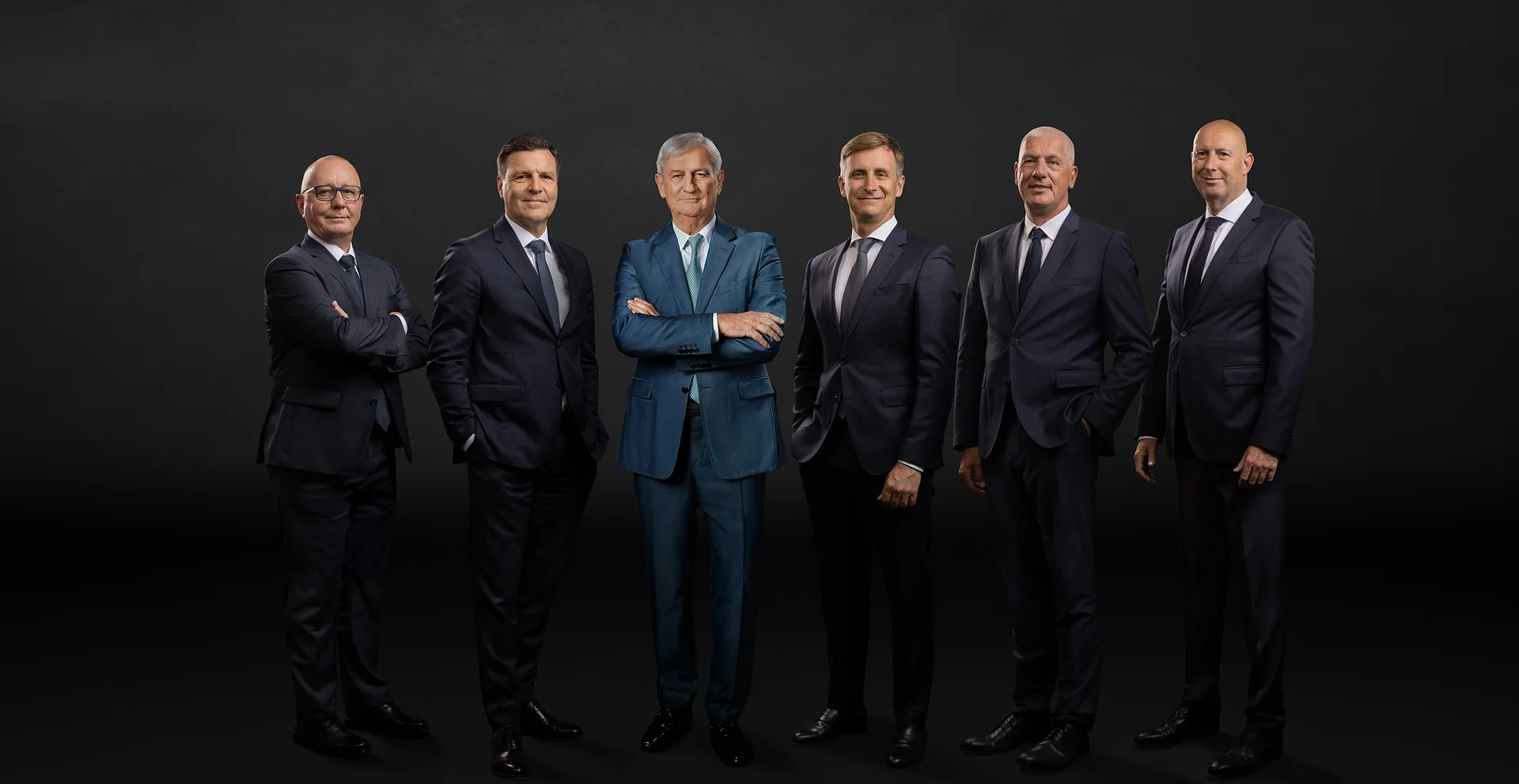 Die Hauptgeschäftsführung vor schwarzem Hintergrund. Sechs Männer lächeln in die Kamera. 