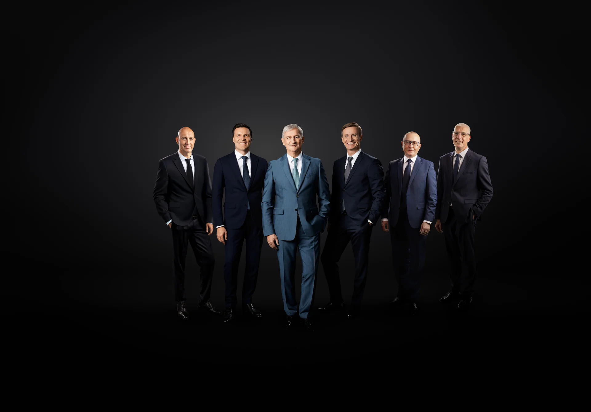 The main management in front of a black background. Six men smile into the camera. 