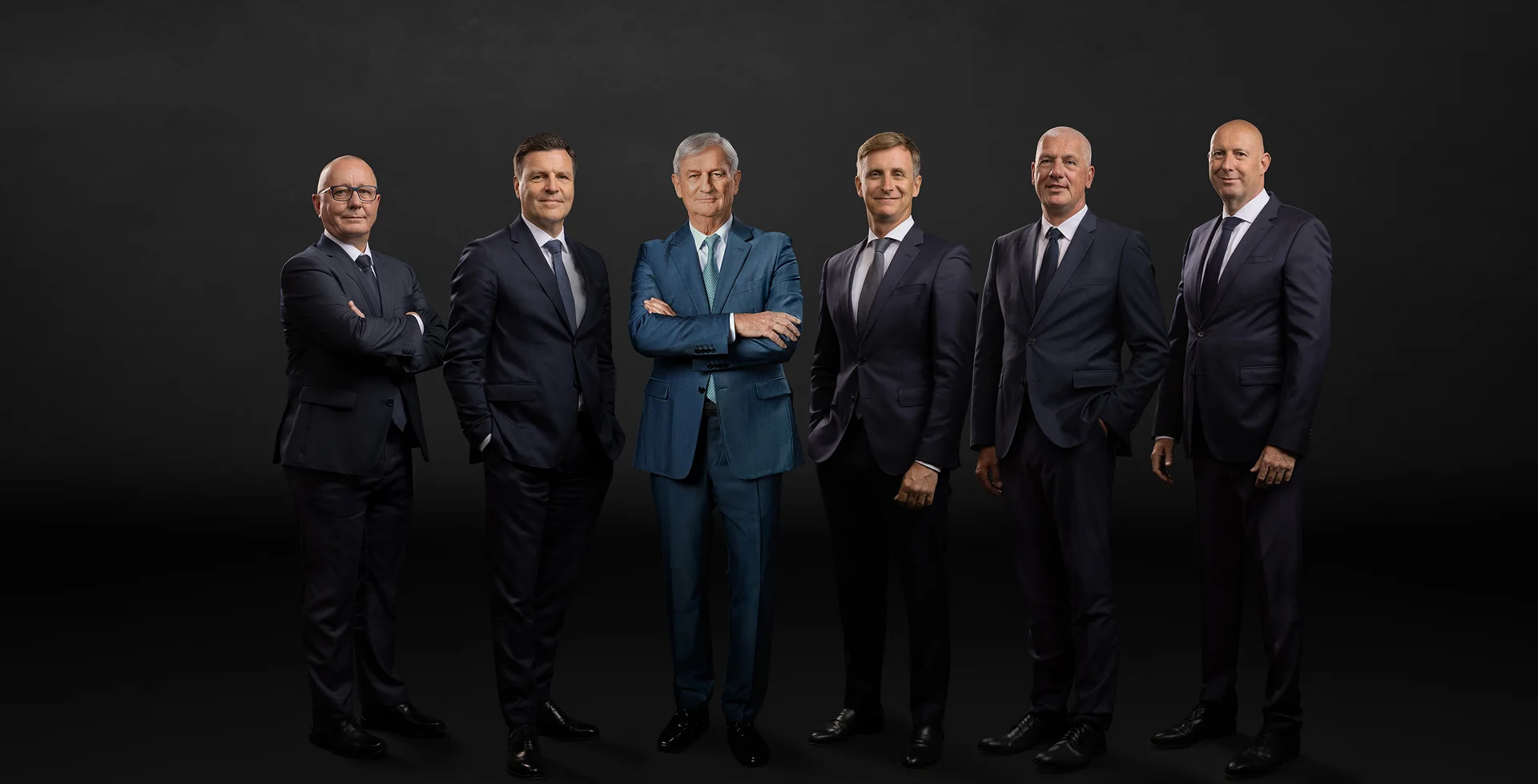 The main management in front of a black background. Six men smile into the camera.