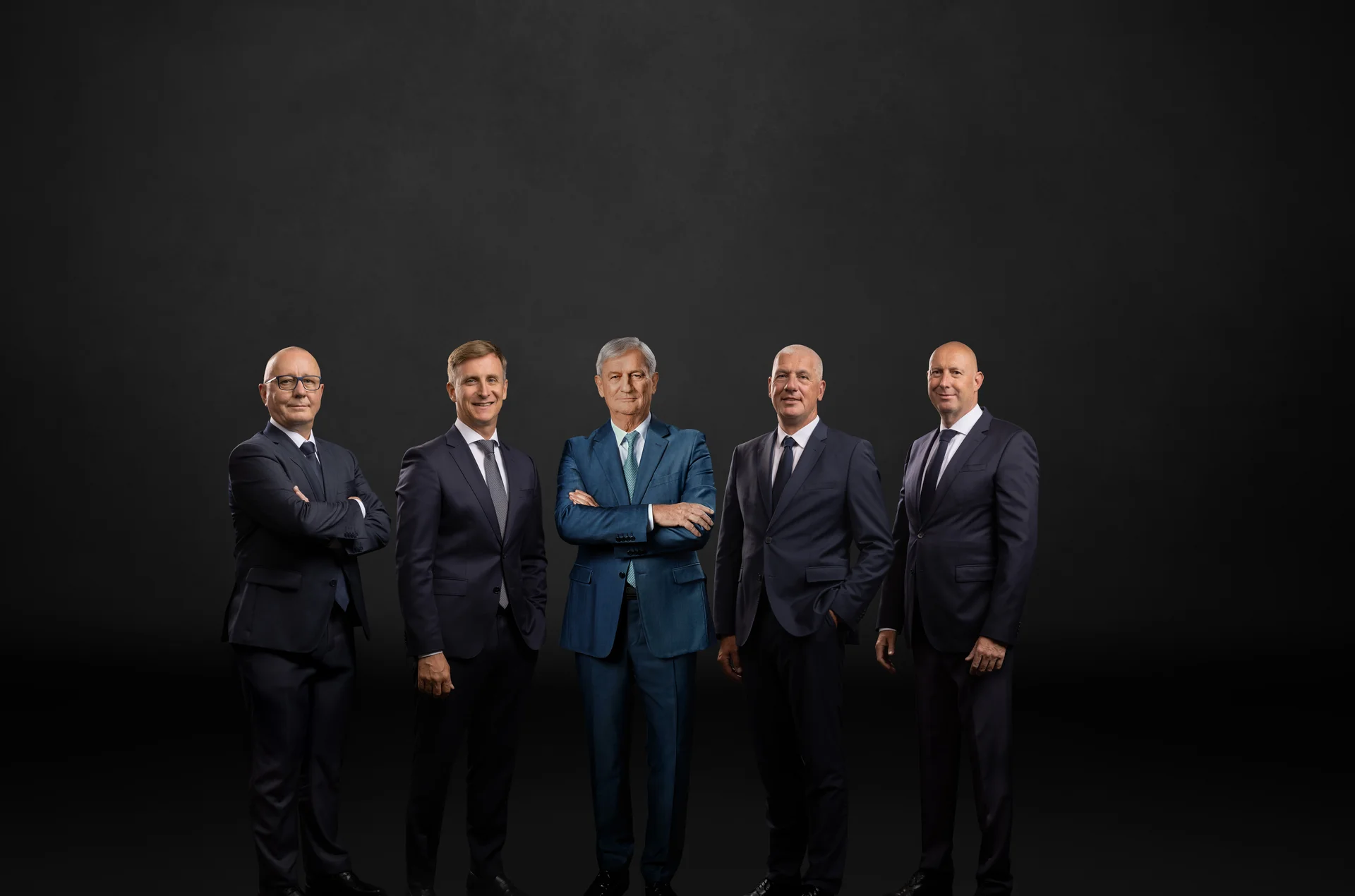 The main management in front of a black background. Six men smile into the camera. 