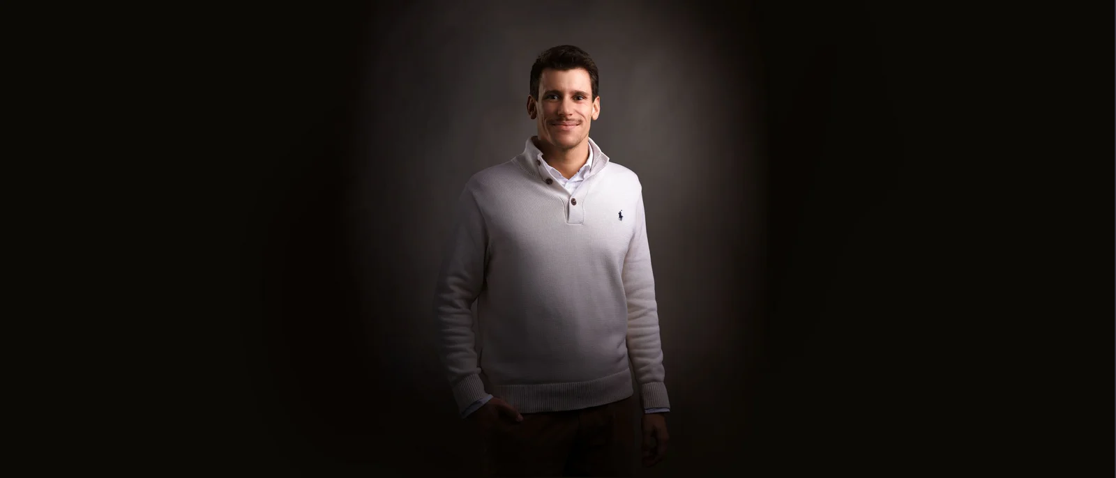 A man in front of a black background smiles at the camera.