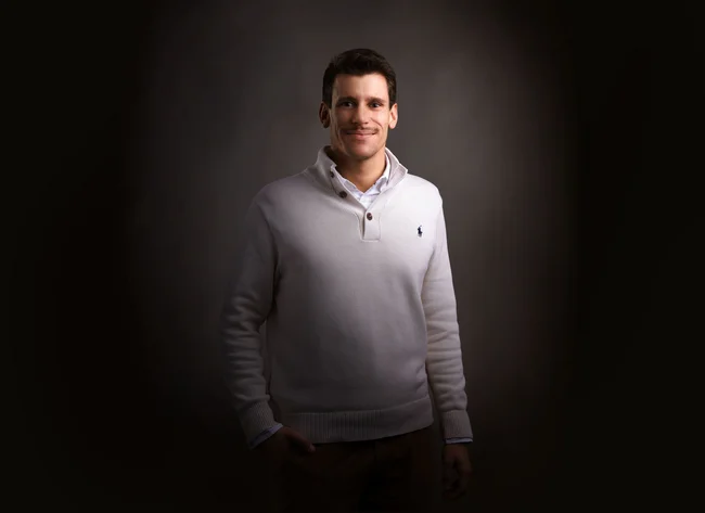 A man in front of a black background smiles at the camera.