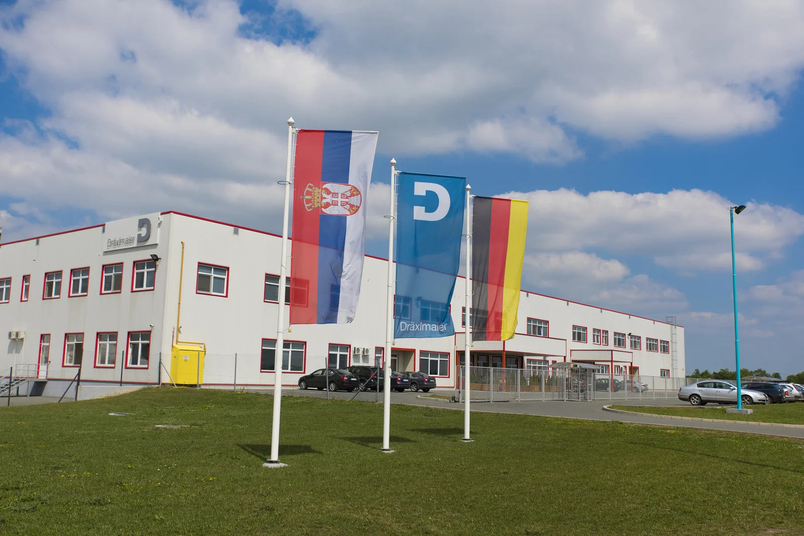 Drei Fahnen vor einem großen, weißen DRÄXLMAIER-Gebäude in Zrenjanin.