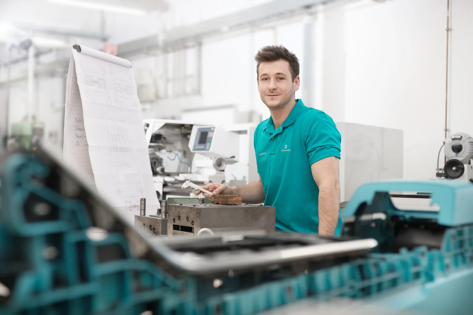 A tool mechanics apprentice at DRÄXLMAIER in Vilsbiburg smiles and works on a workpiece.
