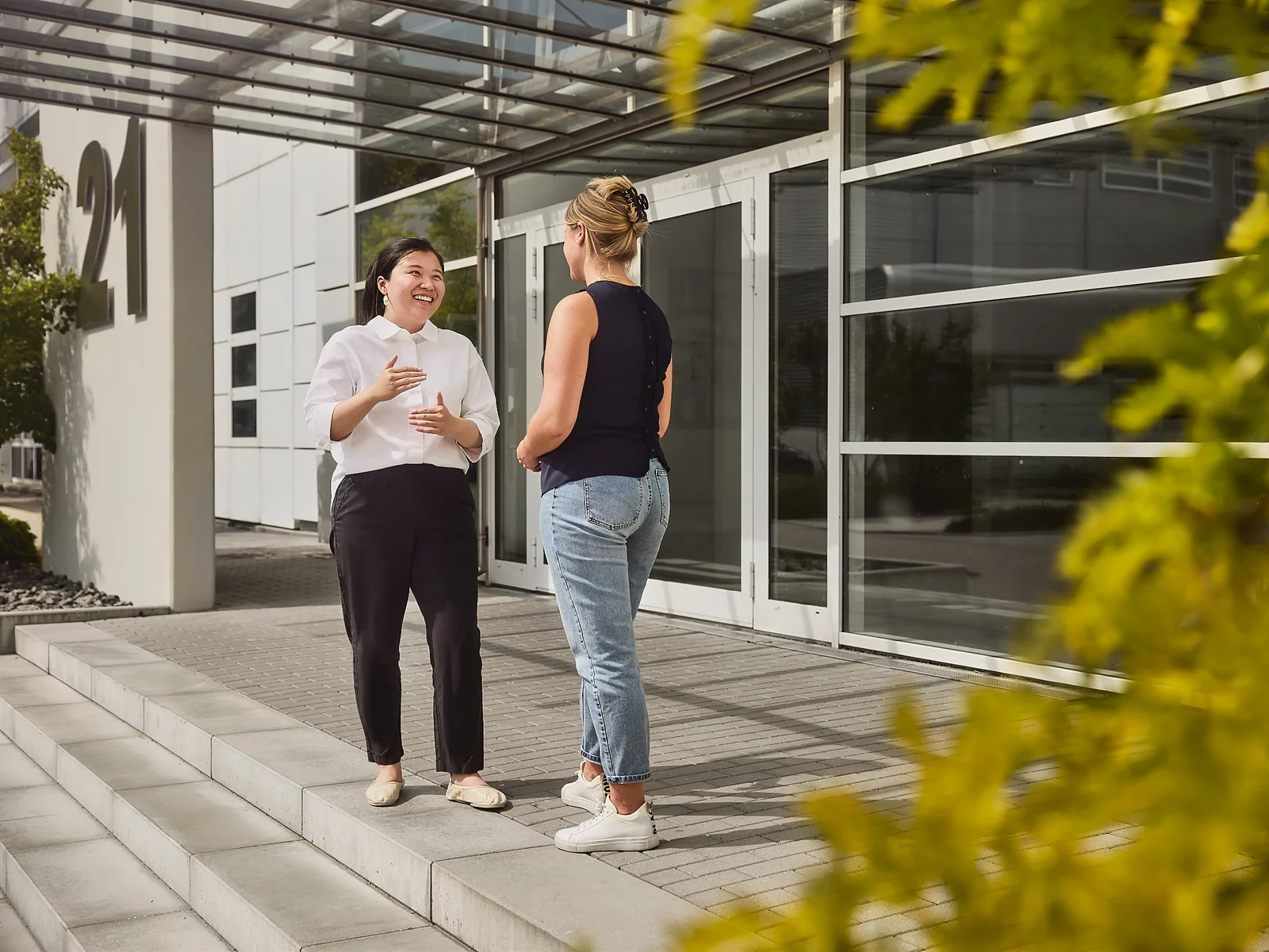Two women are standing in front of a DRÄXLMAIER building and talking.
