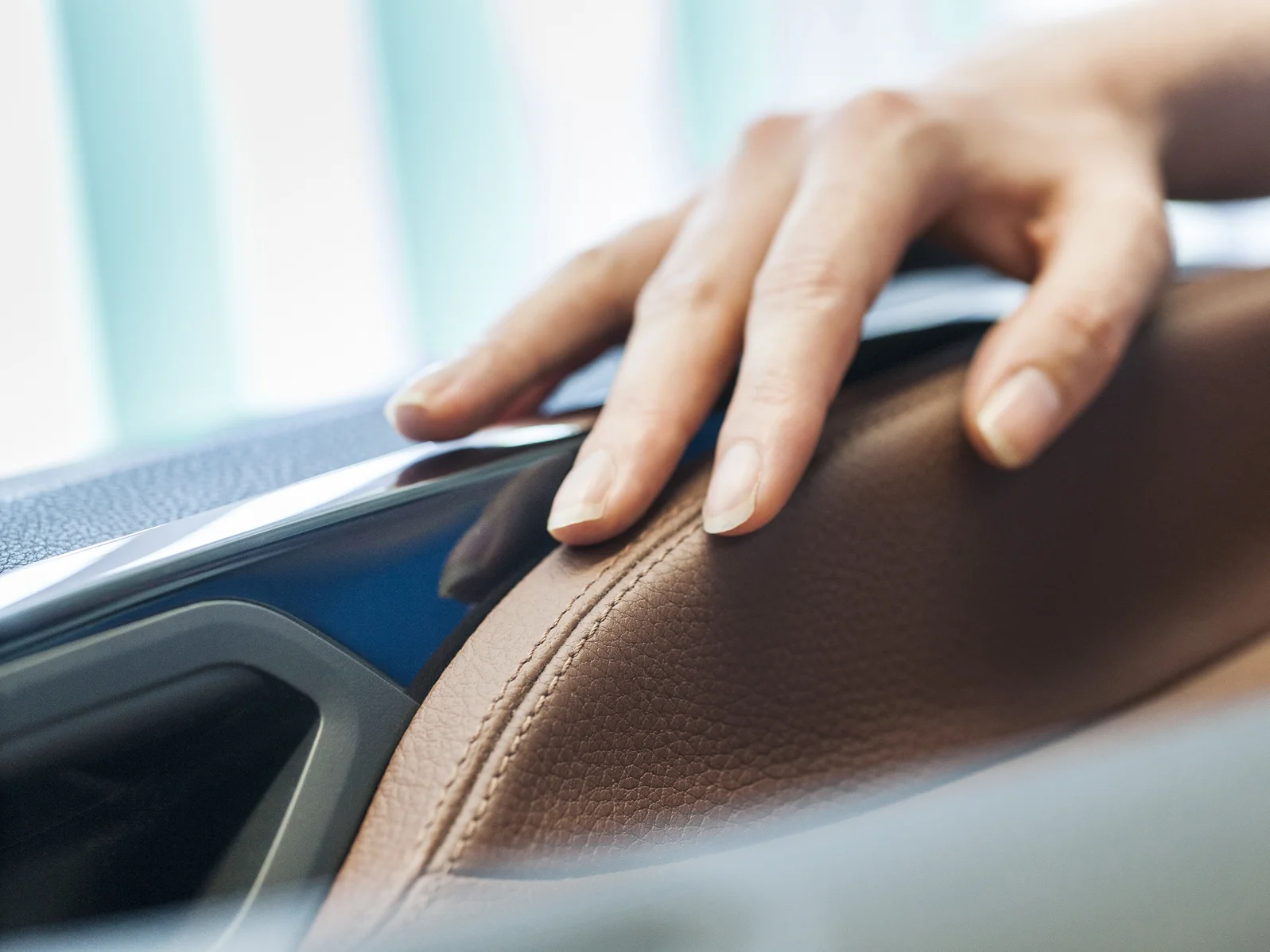 A hand touches a brown, leather-like surface in a vehicle interior.
