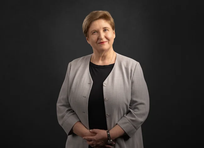 A woman in a grey jacket smiles at the camera.