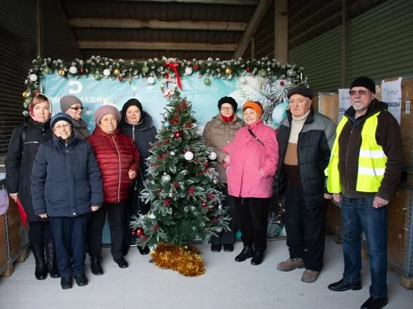 Gruppe von Personen um einen geschmückten Weihnachtsbaum, eine Person trägt eine Warnweste.