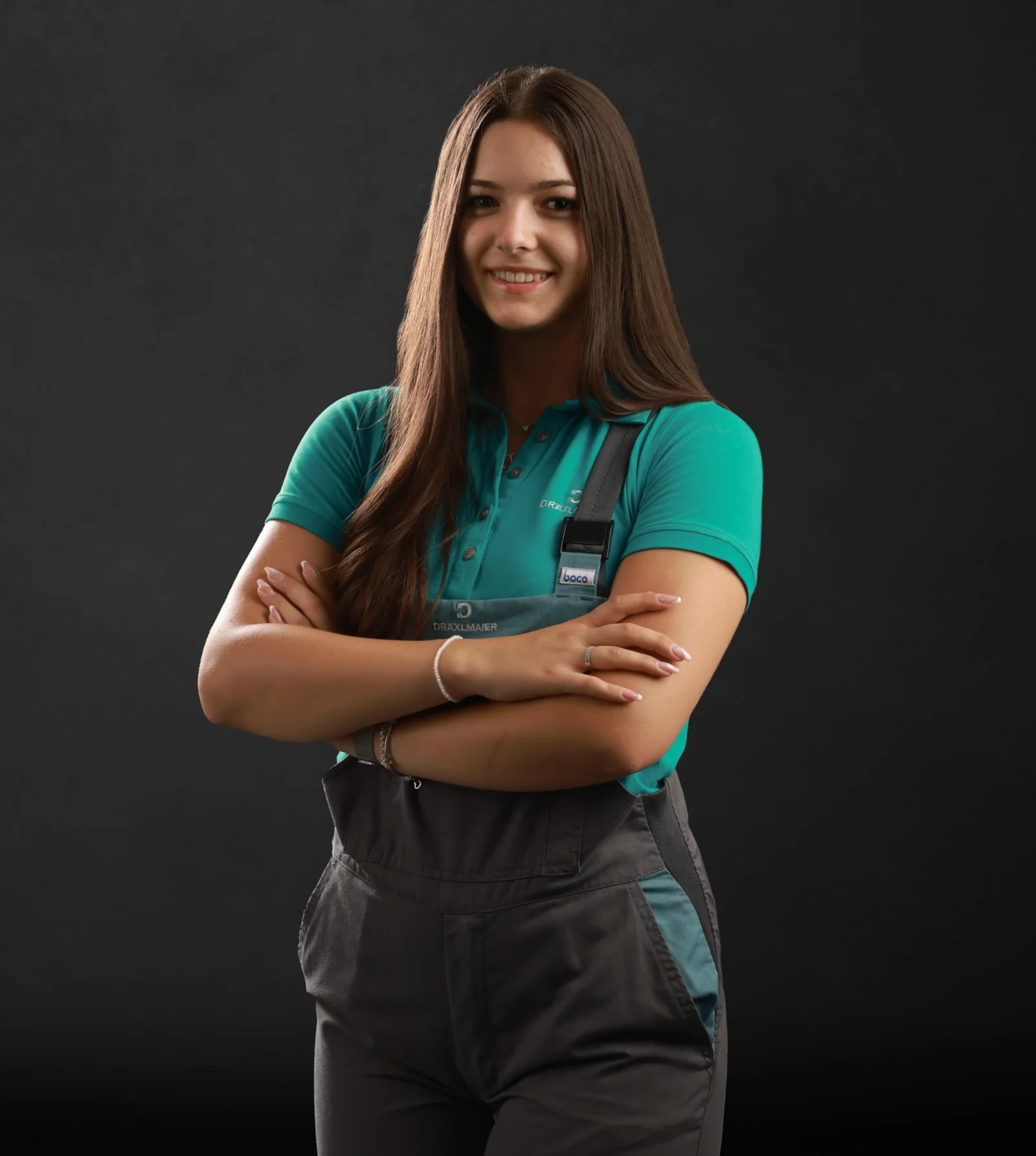 A trainee stands with her arms folded in her work clothes and smiles at the camera.