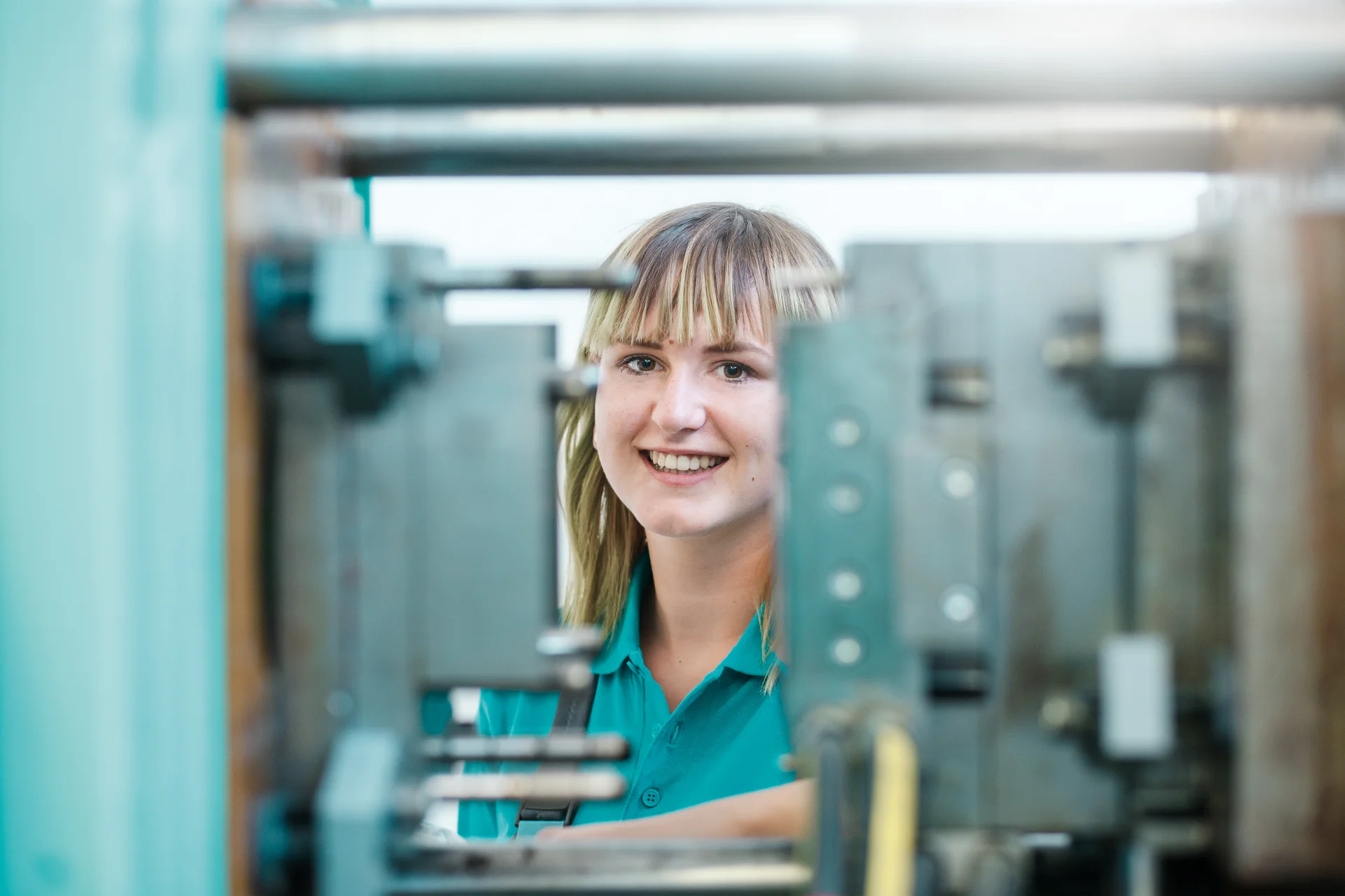 Eine Auszubildende zur Verfahrensmechanikerin lächelt in die Kamera. Im Vordergrund erkennt man die gefertigten Werkstücke.