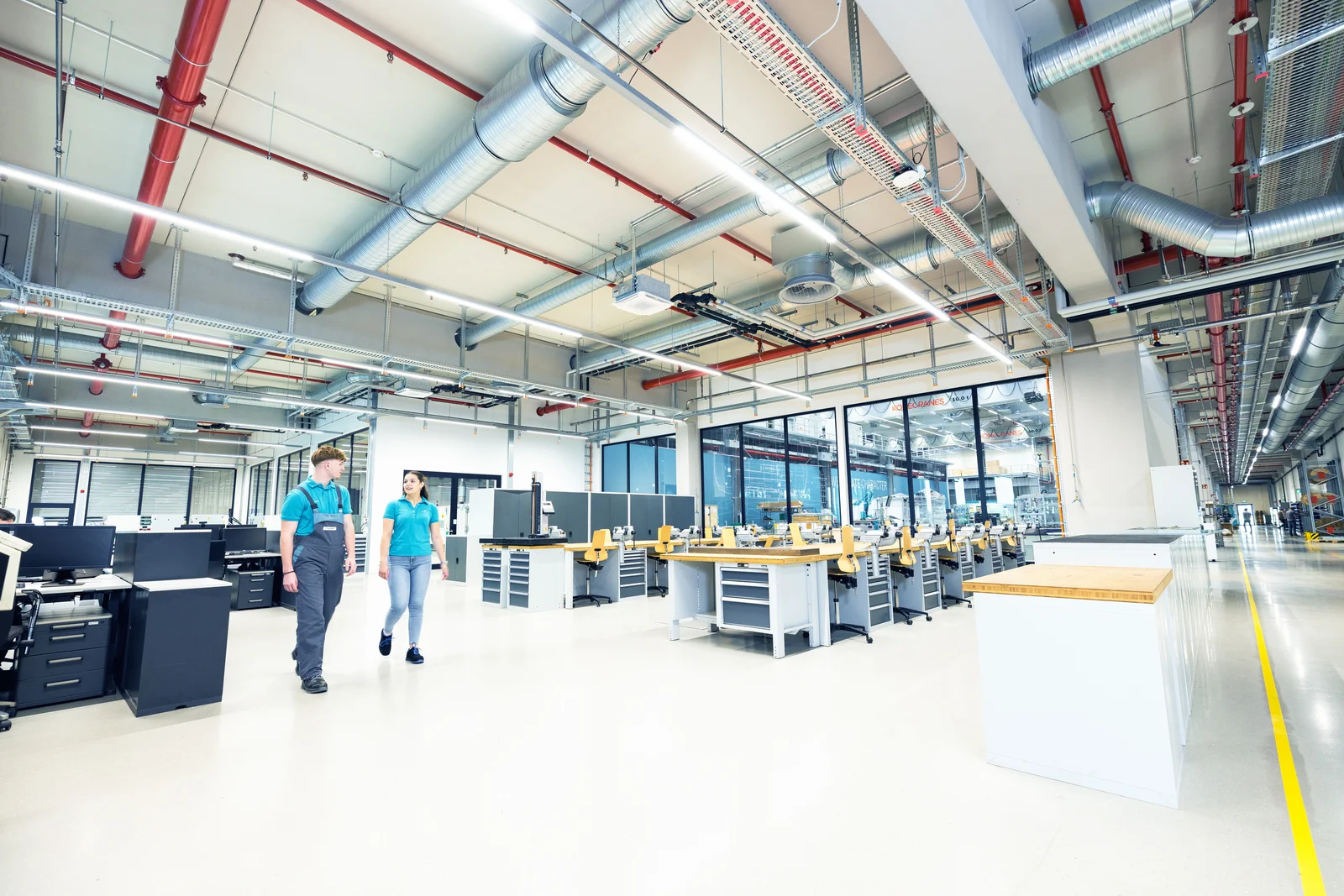 Two trainees walk through the large training workshop and look at each other.