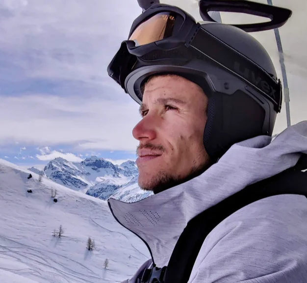 Ein Mann auf einem Skilift mit Skibrille und Skihelm schaut in die Ferne. 