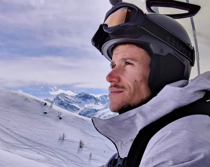 A man on a ski lift wearing ski glasses and a ski helmet looks into the distance.