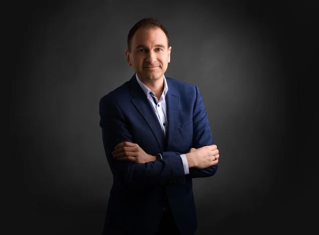 A man with his arms crossed smiles at the camera.