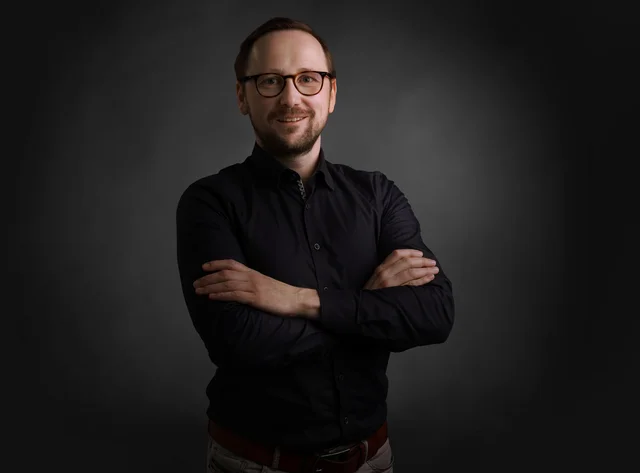 A man with his arms crossed smiles at the camera.