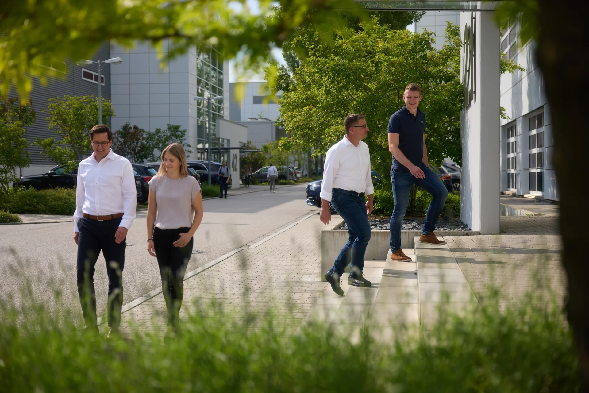 Four people talking on the DRÄXLMAIER premises. Green trees in the background.