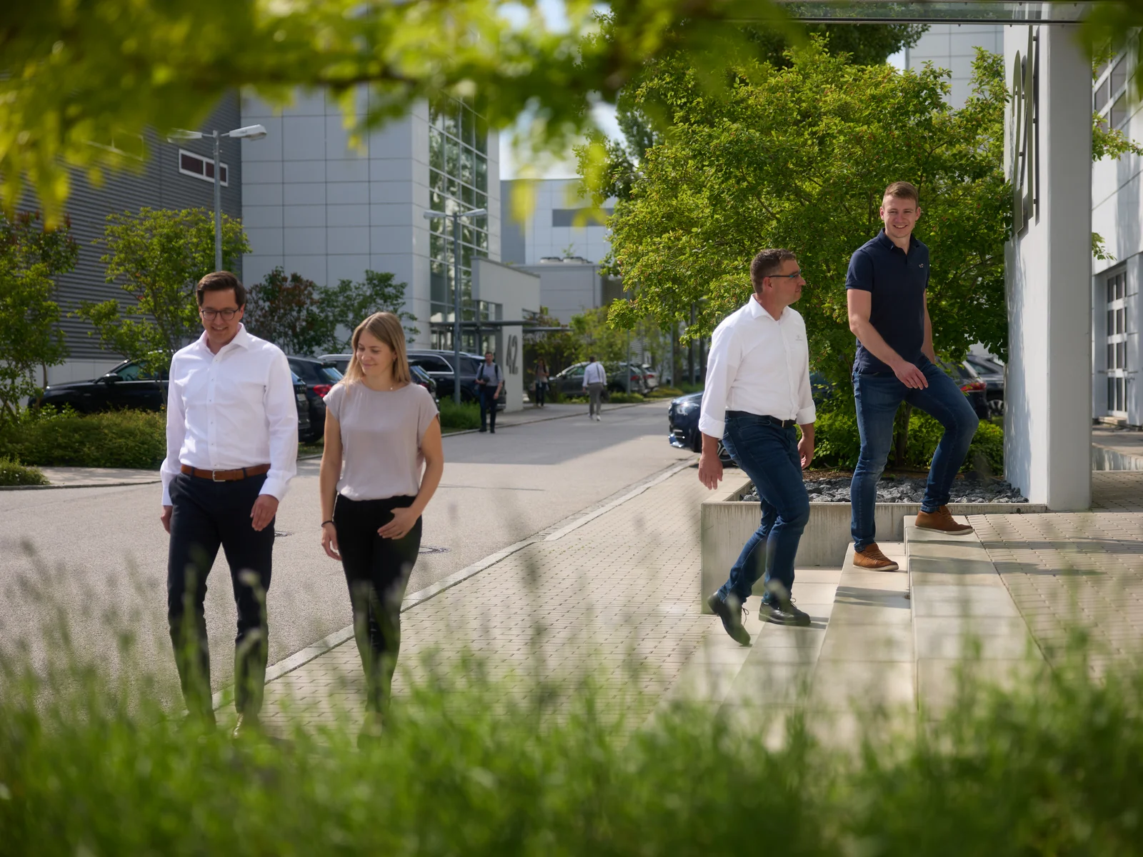 Four people talking on the DRÄXLMAIER premises. Green trees in the background.