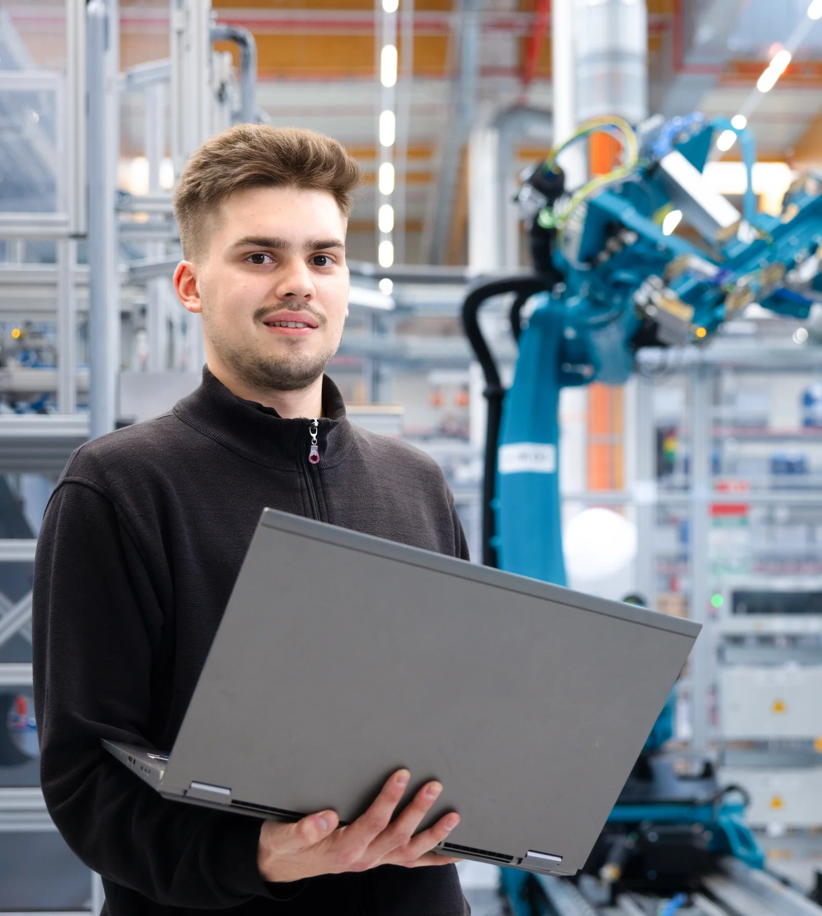 Ein Mann in einer Halle hält einen Laptop in den Händen.