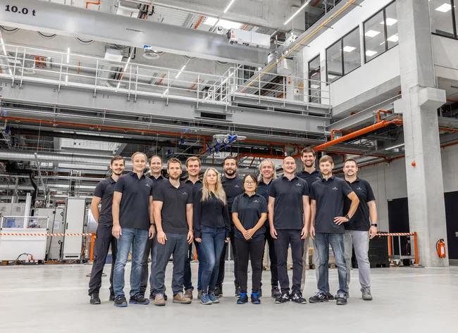 Ein Gruppenfoto mit lächelnden DRÄXLMAIER Produktionsmitarbeitern in einer Halle. 