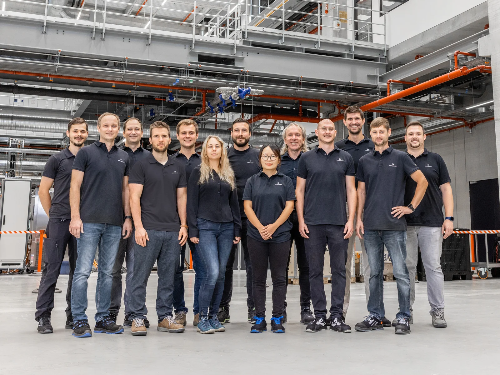 A group photo with smiling DRÄXLMAIER production employees in a hall. 