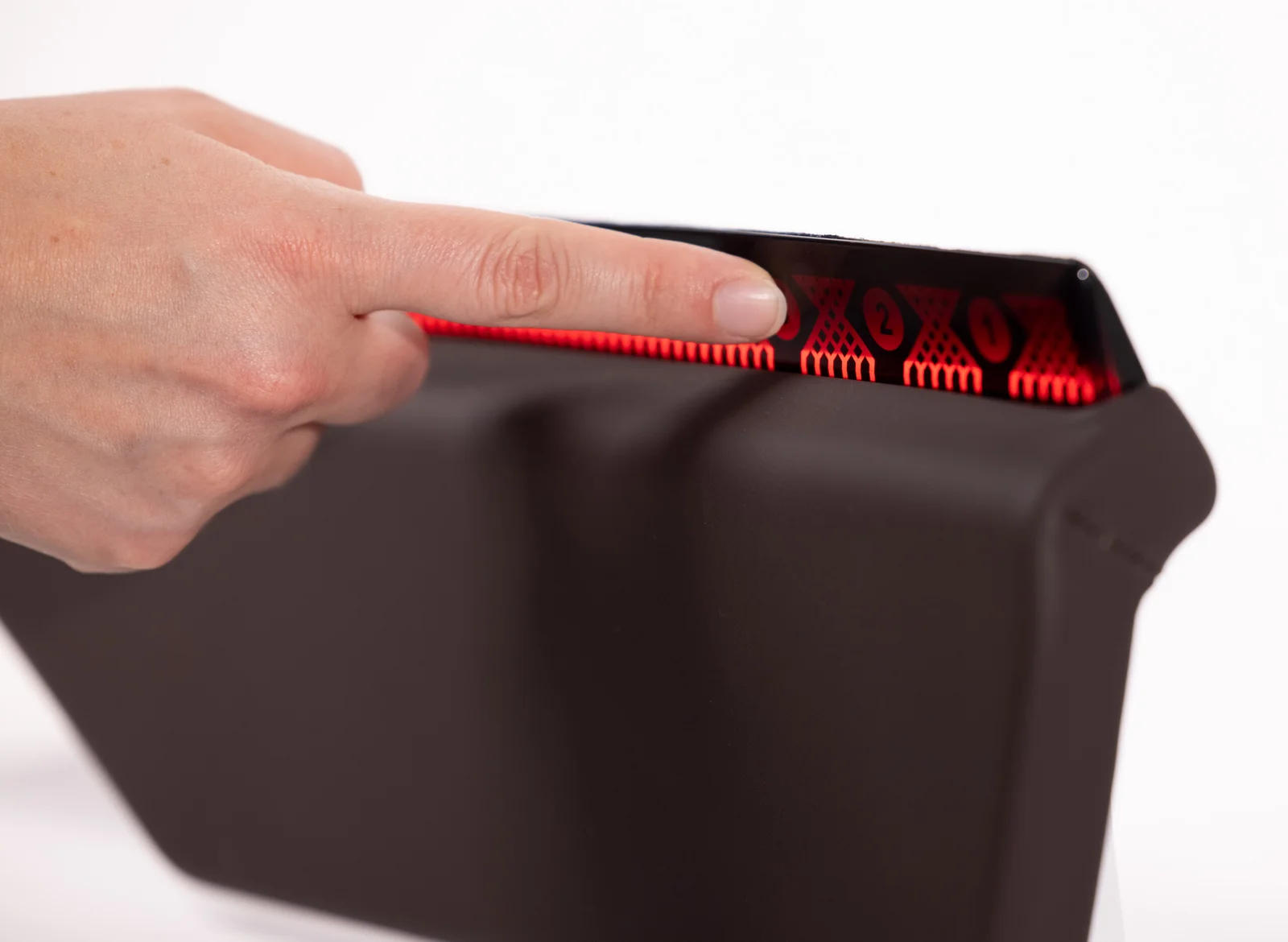 A hand presses on a red, illuminated display with symbols and numbers on a black touchscreen.