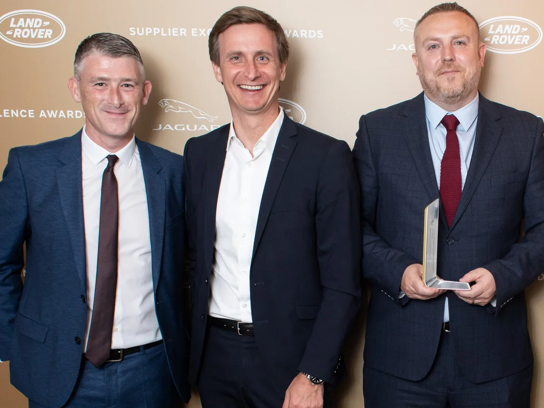 Four people smile at the camera. The JLR Suppliers Excellence Award is presented. 