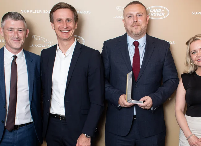 Four people smile at the camera. The JLR Suppliers Excellence Award is presented. 