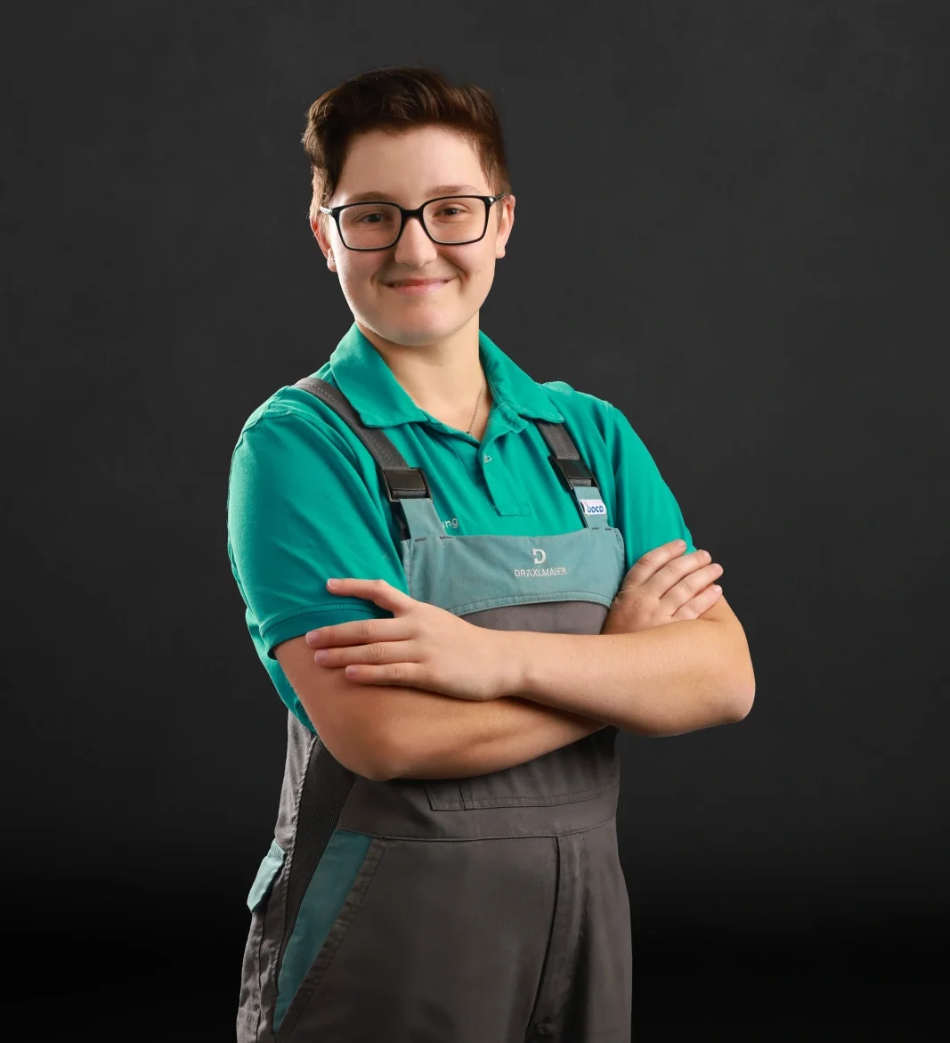 A trainee stands with her arms folded in her work clothes and smiles at the camera.