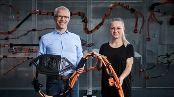 Ein Mann und eine Frau lächeln in die Kamera. Sie halten einen Teil eines Kabelbaums in den Händen.