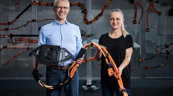A man and a woman smile at the camera. They are holding part of a cable harness in their hands.