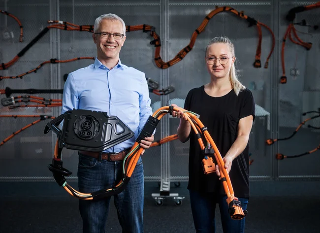 Ein Mann und eine Frau lächeln in die Kamera. Sie halten einen Teil eines Kabelbaums in den Händen.