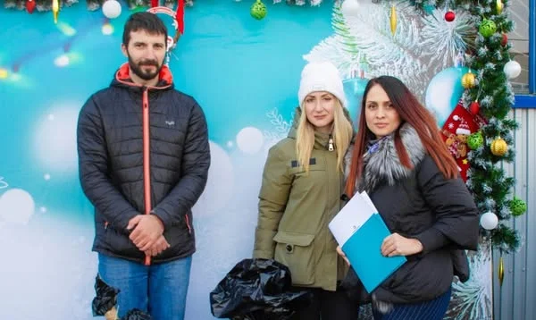 Drei Personen vor weihnachtlicher Dekoration mit Müllsäcken und einem blauen Ordner.