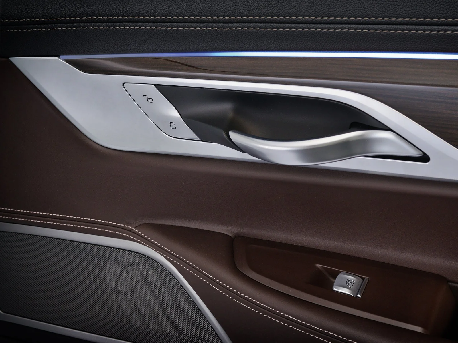 Interior panelling of a car door with silver door handle, buttons, switches, white decorative stitching and loudspeaker.