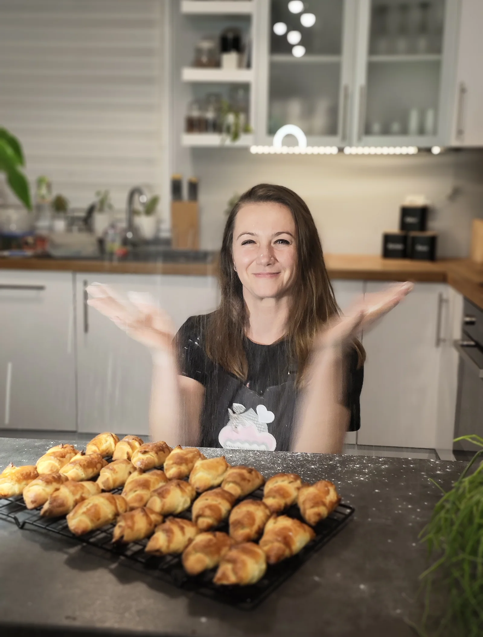 A DRÄXLMAIER employee is sitting in a kitchen. In front of her is a tray of croissants. 