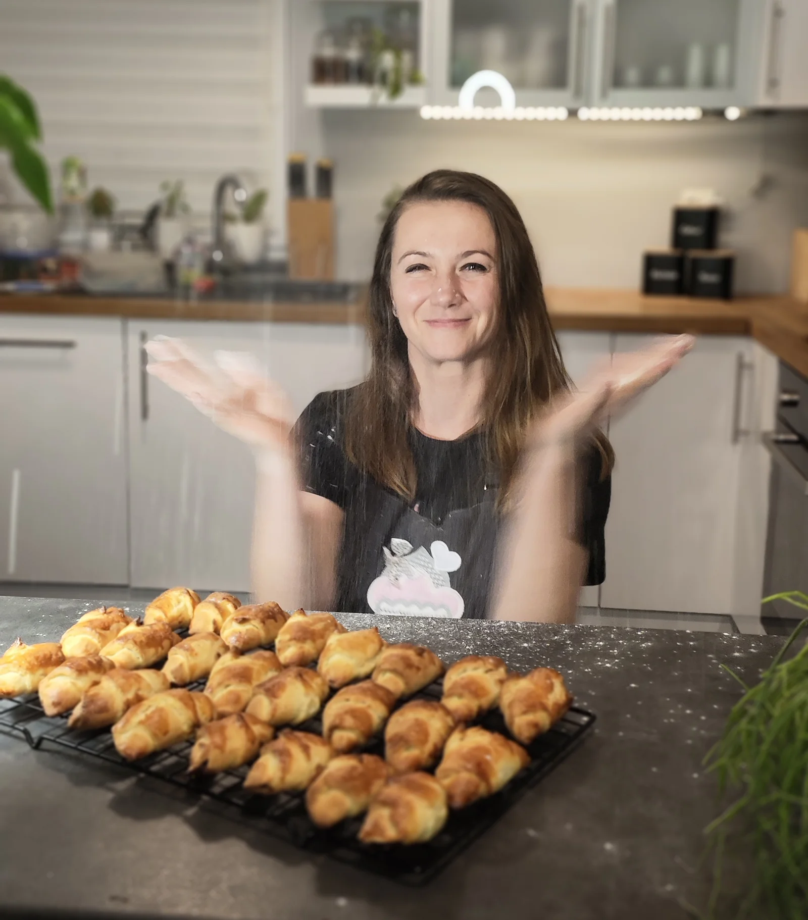 Eine Mitarbeiterin von DRÄXLMAIER sitzt in einer Küche. Vor ihr steht ein Tablett mit Croissants. 