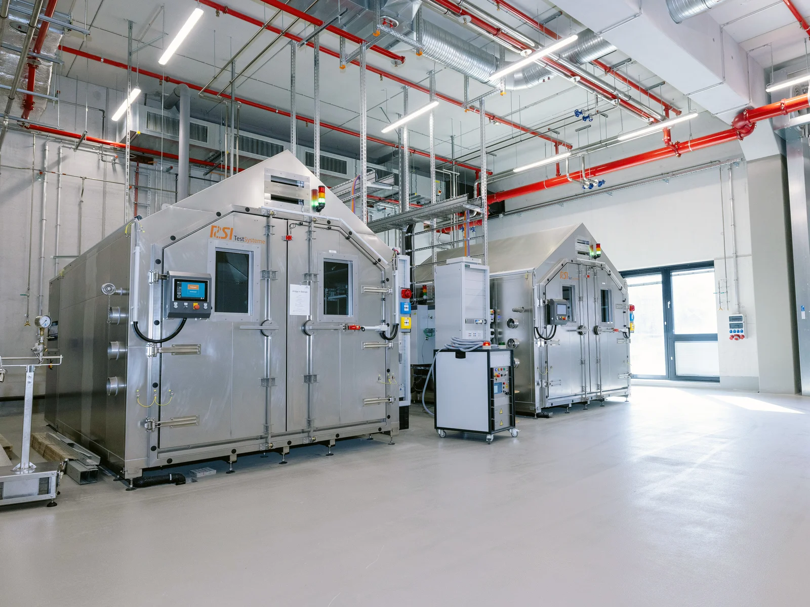 Large industrial machine in a spacious facility with high ceilings and various pipes and cables.
