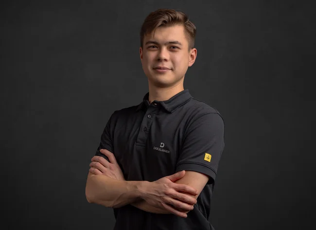 A young man smiles into the camera with his arms crossed.