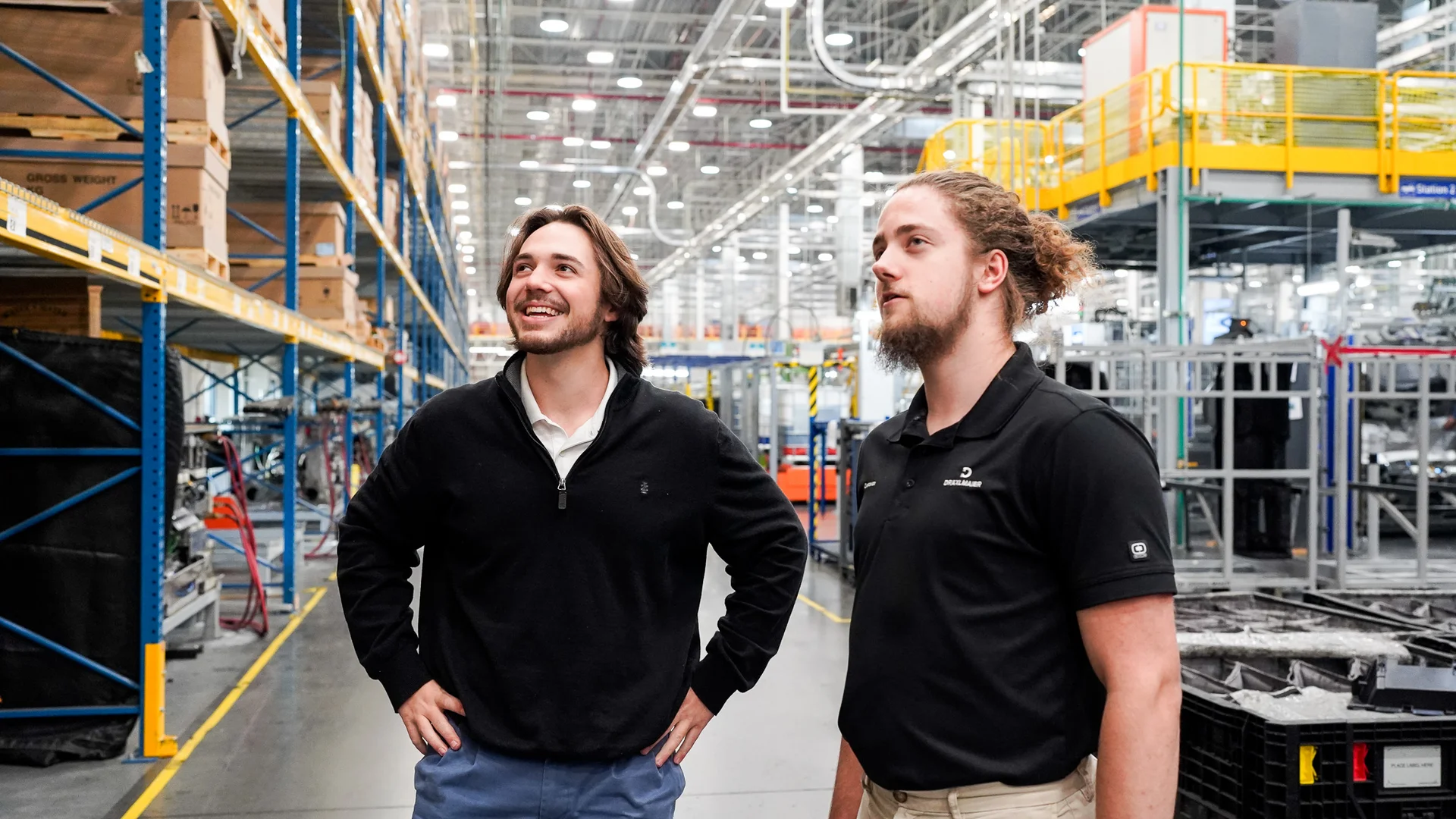 DRÄXLMAIER employees stand in a warehouse and look at a shelf.