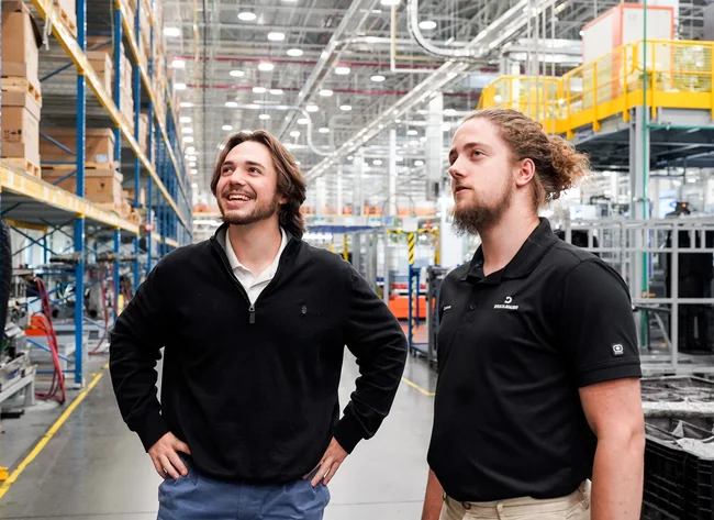 DRÄXLMAIER employees stand in a warehouse and look at a shelf.
