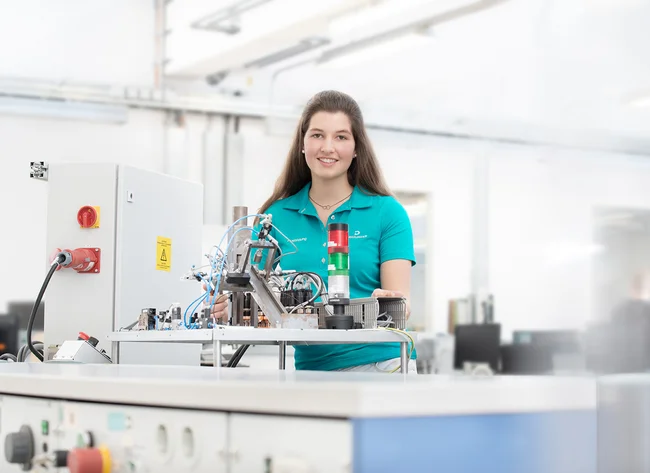Eine Auszubildende in der Elektronik bei DRÄXLMAIER in Vilsbiburg lächelt in die Kamera und arbeitet an einem Schaltkreis.