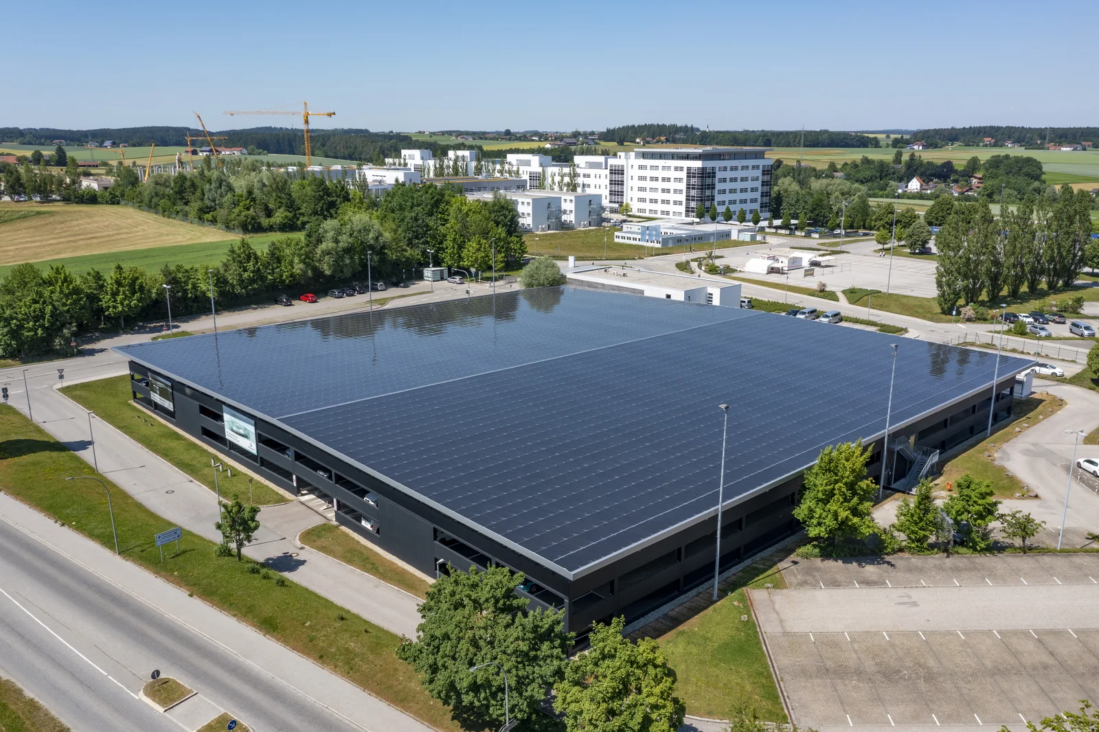 Das Parkdeck in Vilsbiburg mit Solarpaneelen auf dem Dach, umgeben von Straßen, Bäumen und weiteren Gebäuden.