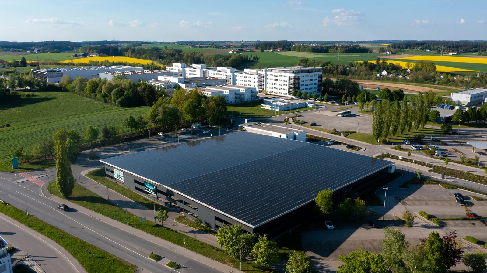 Das Parkdeck in Vilsbiburg mit Solarpaneelen auf dem Dach, umgeben von Straßen, Bäumen und weiteren Gebäuden.
